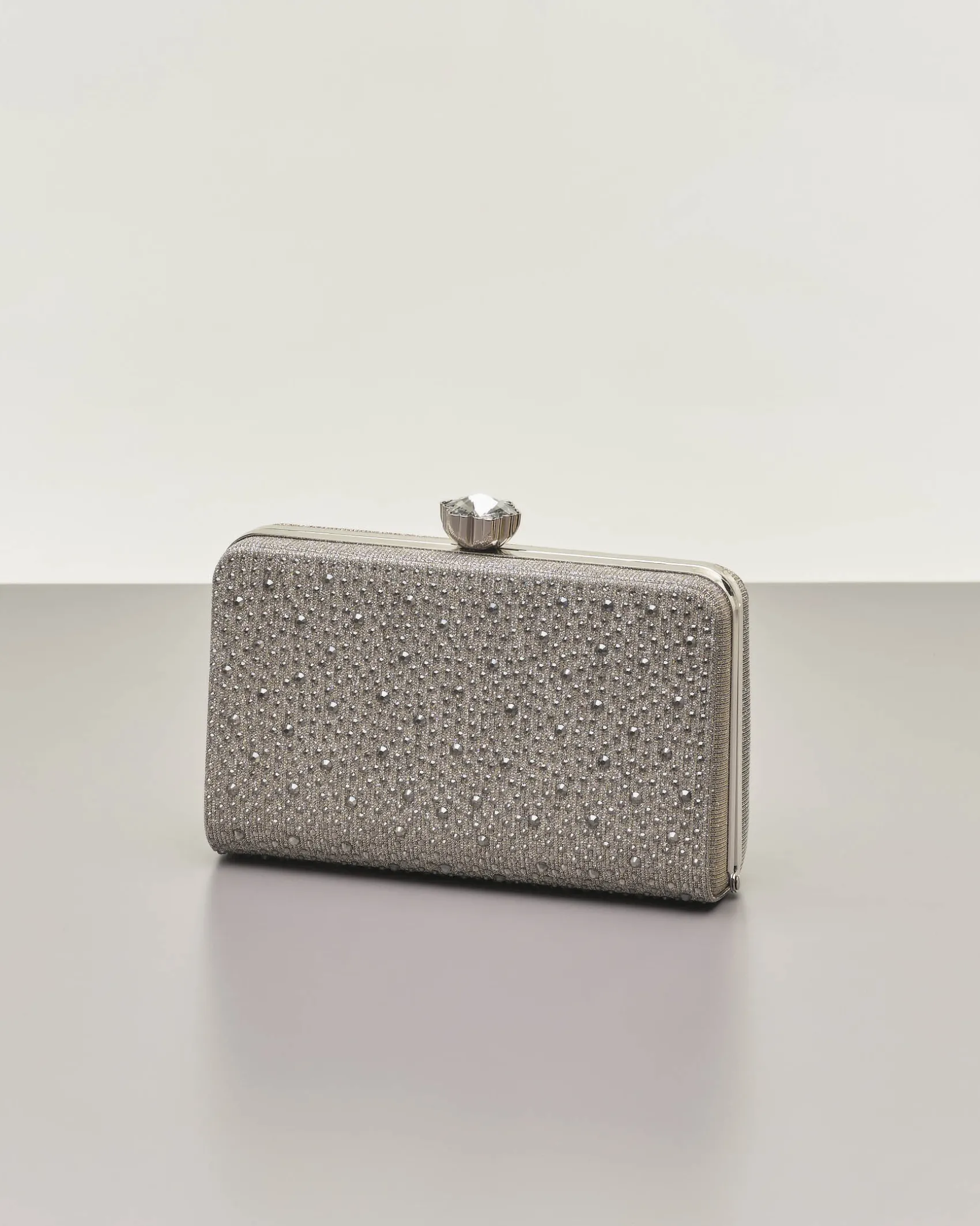 Clutch rigida color grigia in lurex con strass tono su tono applicati sul davanti e chiusura a gioiello a scatto
